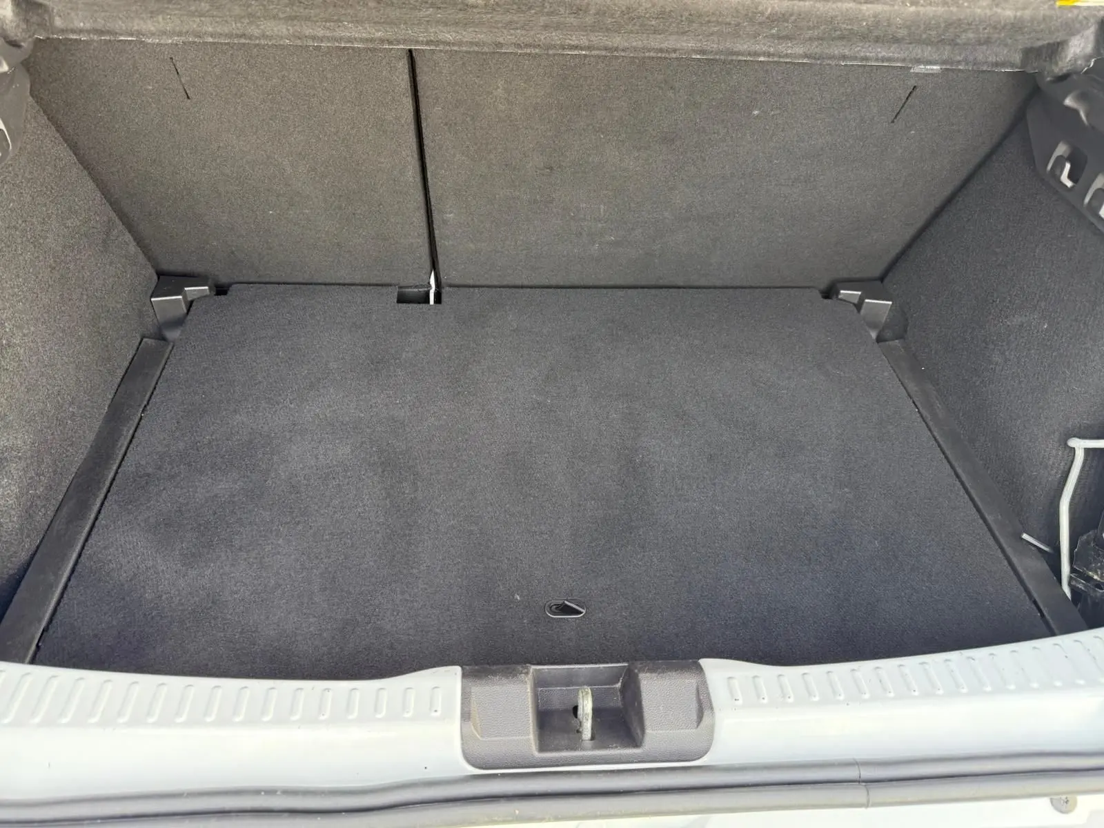 Coffre vide vu de l'arrière d'une Dacia Sandero blanche 2023, avec revêtement noir et seuil de chargement clair.