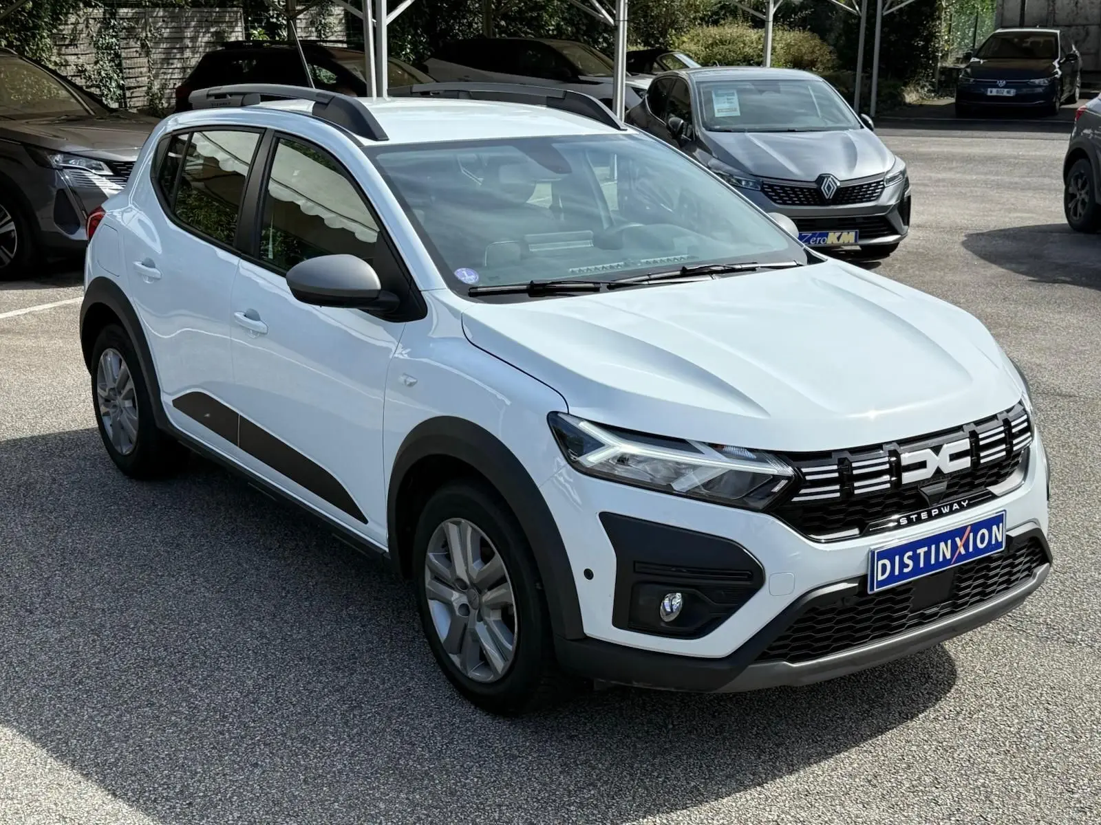 Vue 3/4 avant d'une Dacia Sandero Stepway blanche 2023 avec calandre noire et barres de toit noires.