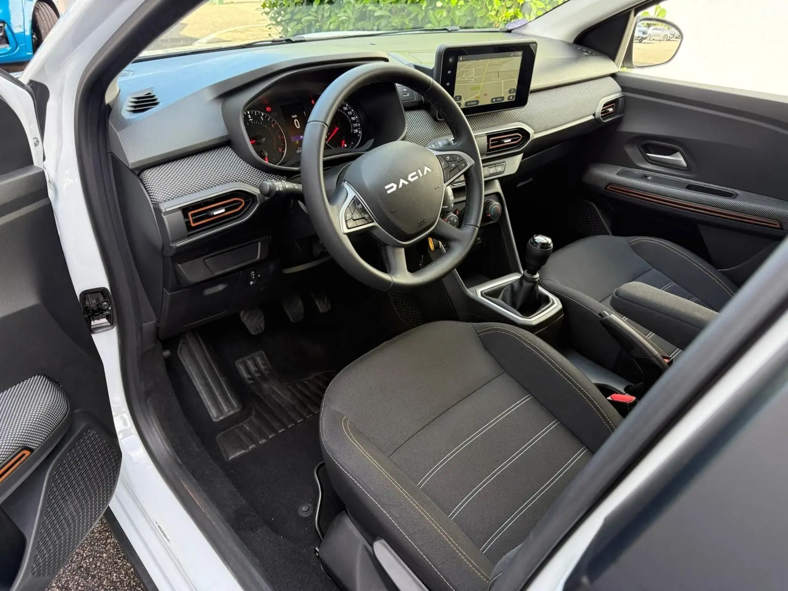 Intérieur avant droit d'une Dacia Sandero blanche 2023, volant multifonction, écran tactile et sièges noirs avec surpiqûres.