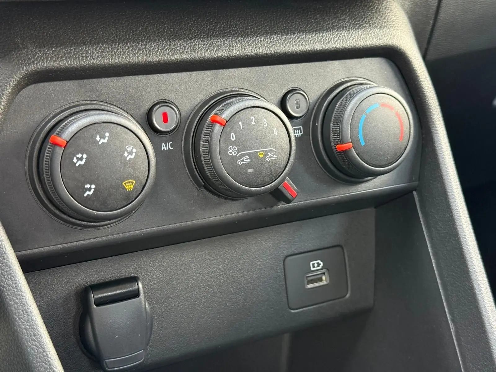 Gros plan sur les commandes de climatisation et port USB du tableau de bord noir de la Dacia Sandero blanche 2023.
