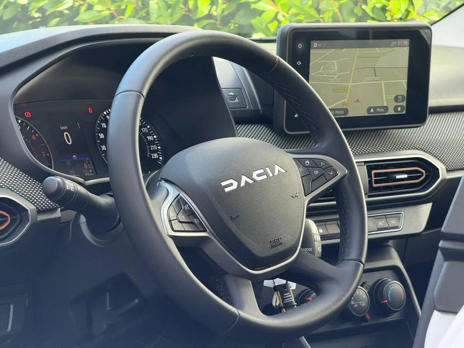 Vue rapprochée du volant Dacia Sandero 2023 avec tableau de bord numérique et écran tactile GPS allumé.