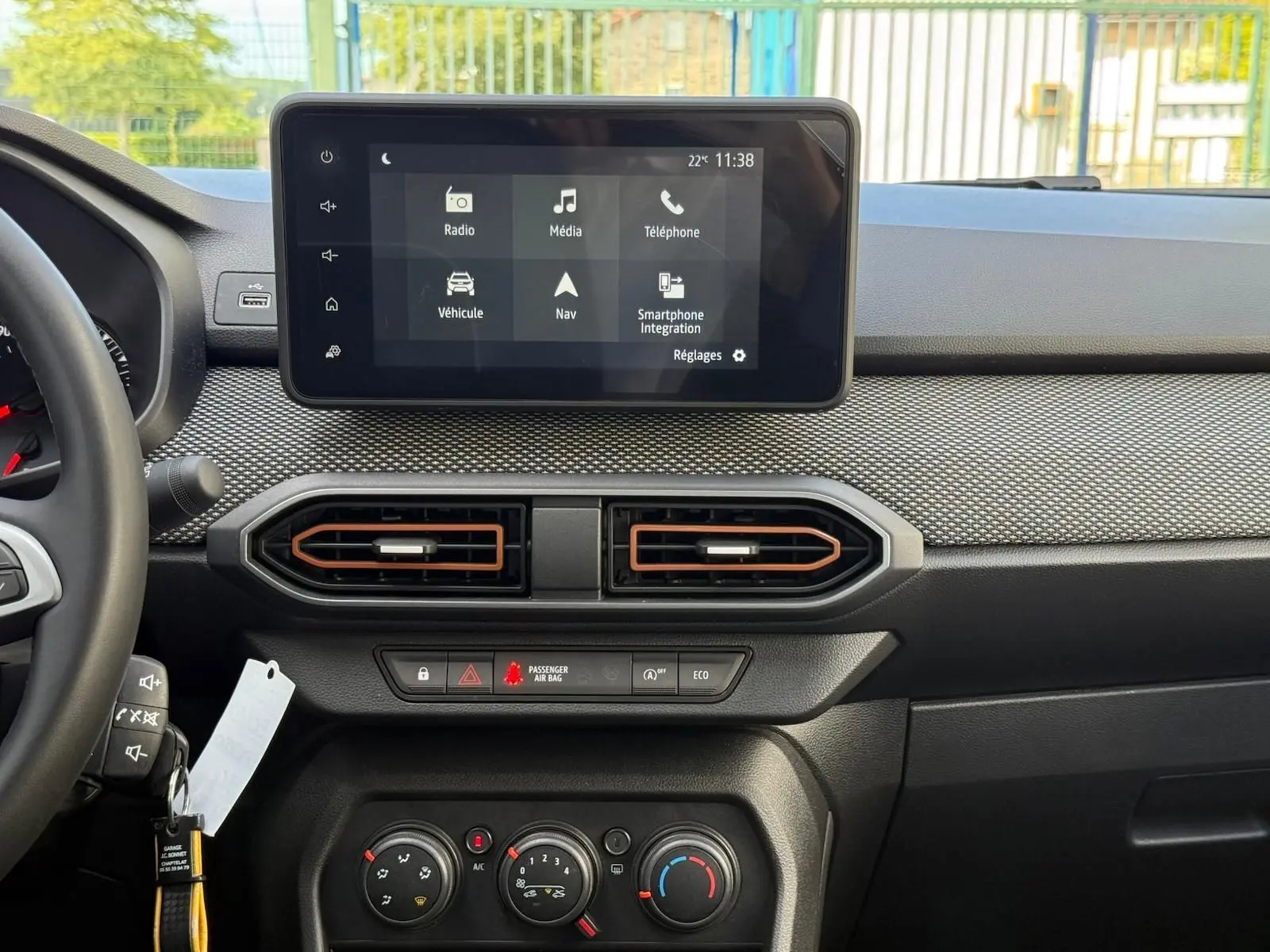 Tableau de bord de la Dacia Sandero blanche 2023, vue frontale centrée sur l'écran tactile et les commandes de climatisation.