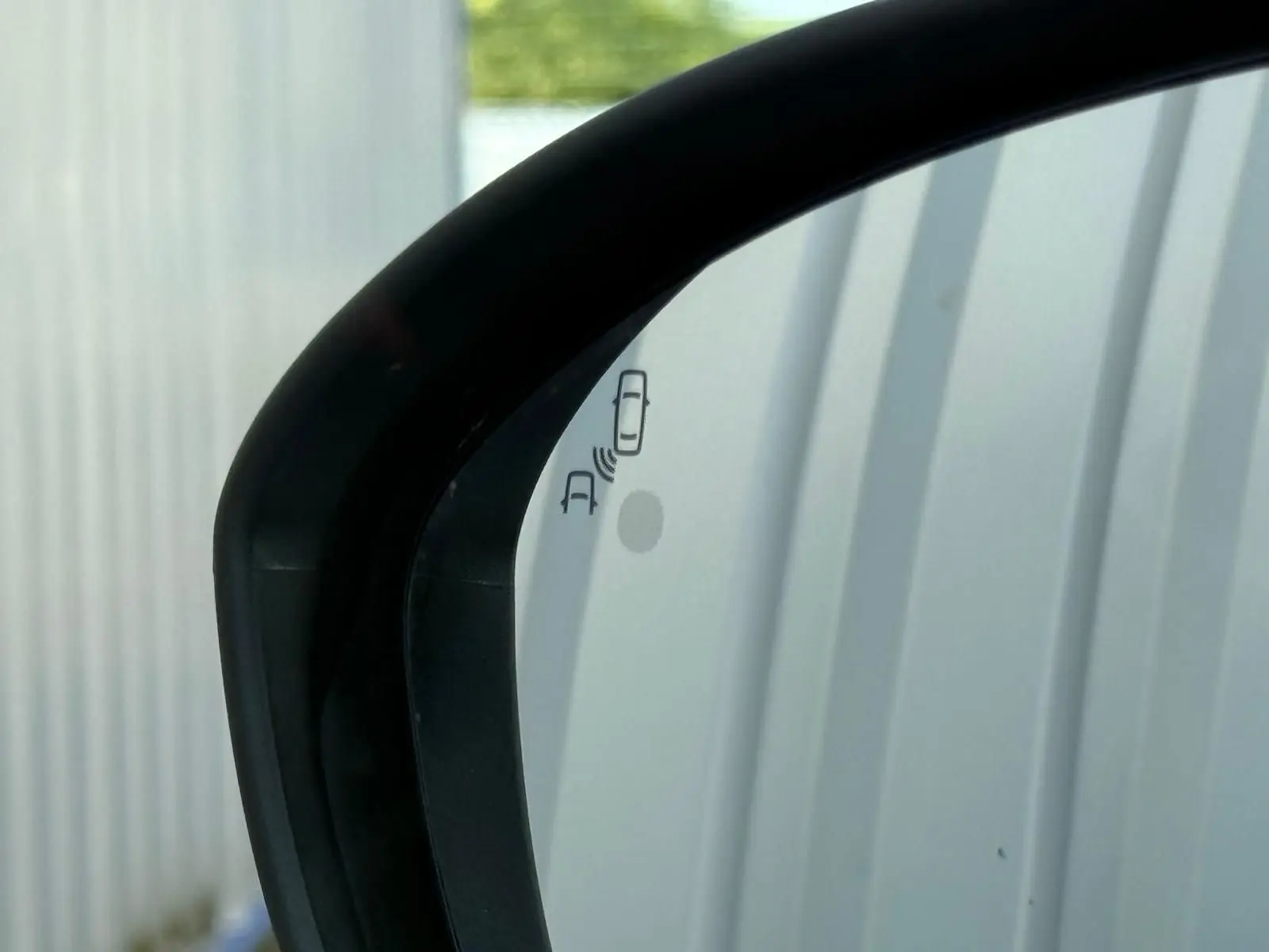 Gros plan sur le rétroviseur extérieur droit noir d'une Dacia Sandero blanche 2023 avec alerte d'angle mort visible.