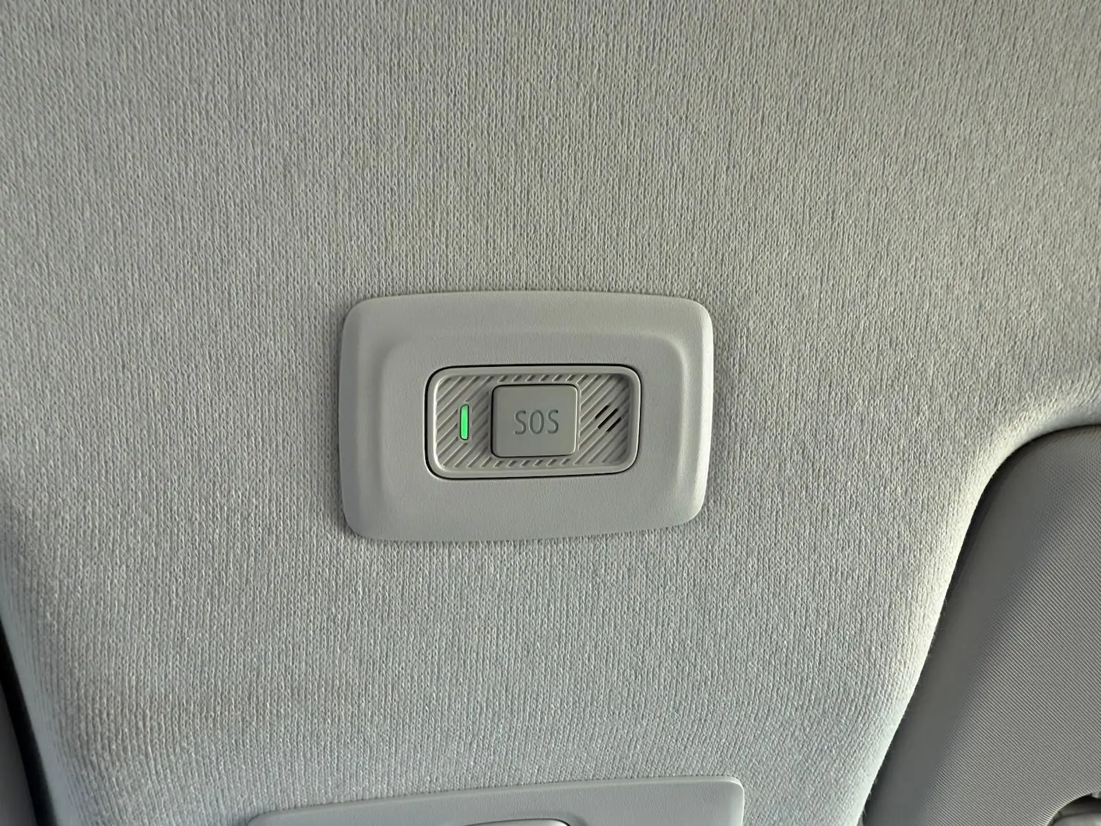 Bouton SOS éclairé en vert sur le plafond intérieur gris clair d'une Dacia Sandero blanche 2023.