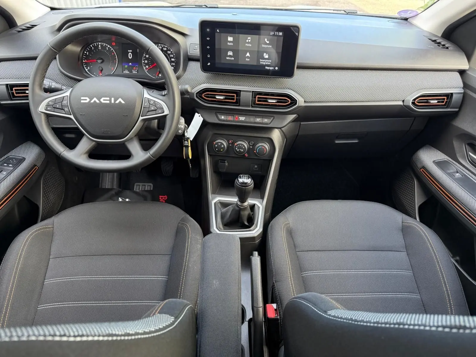 Vue intérieure avant du tableau de bord et volant Dacia Sandero 2023 avec écran tactile et boîte manuelle.