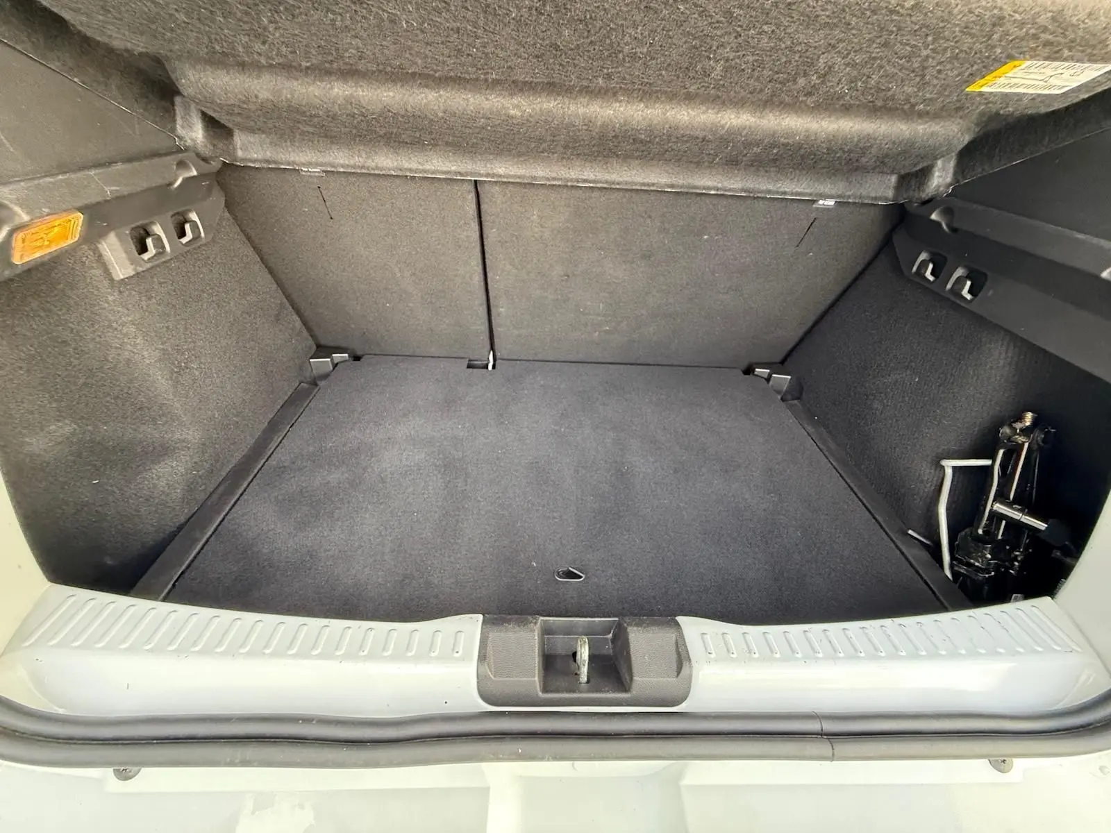 Coffre ouvert d'une Dacia Sandero blanche 2023, vue de l'arrière montrant l'espace de chargement vide et le cric.