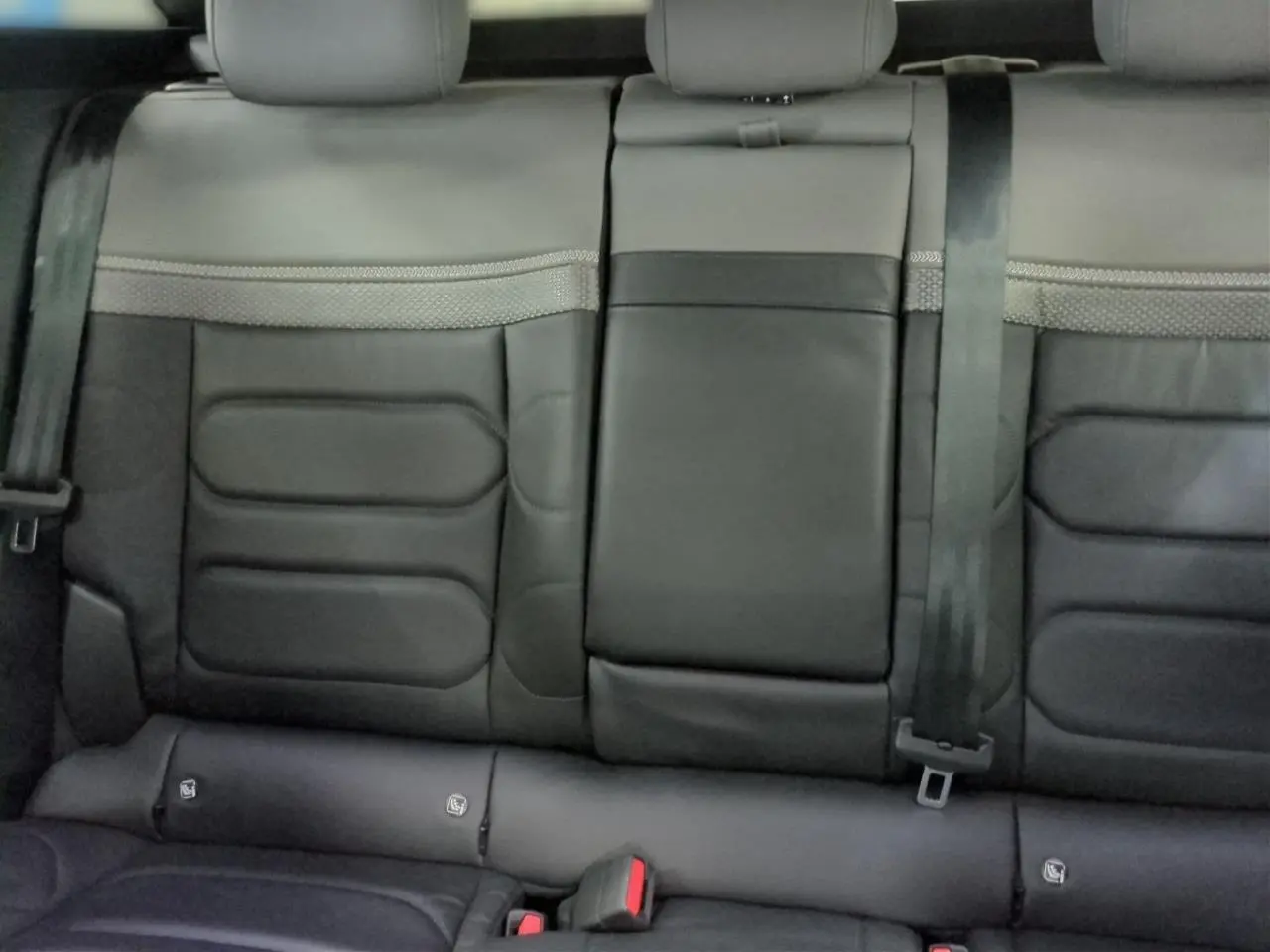 Vue rapprochée des sièges arrière en cuir noir de la Citroën C5 X 2024 avec ceinture de sécurité et accoudoir central rabattable.