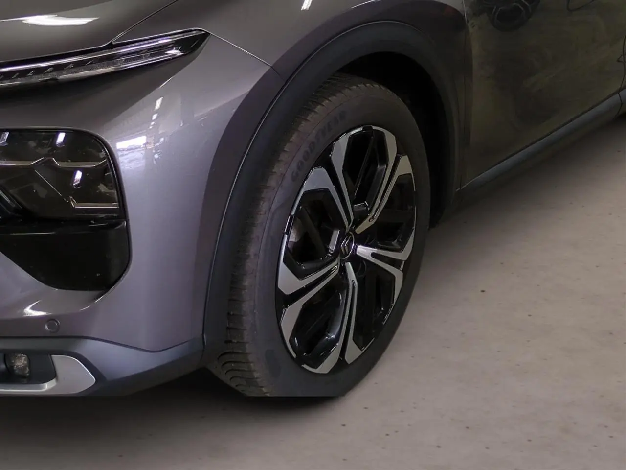 Gros plan sur la roue avant droite et le pare-chocs avant gris Platinium du Citroën C5 X 2024.