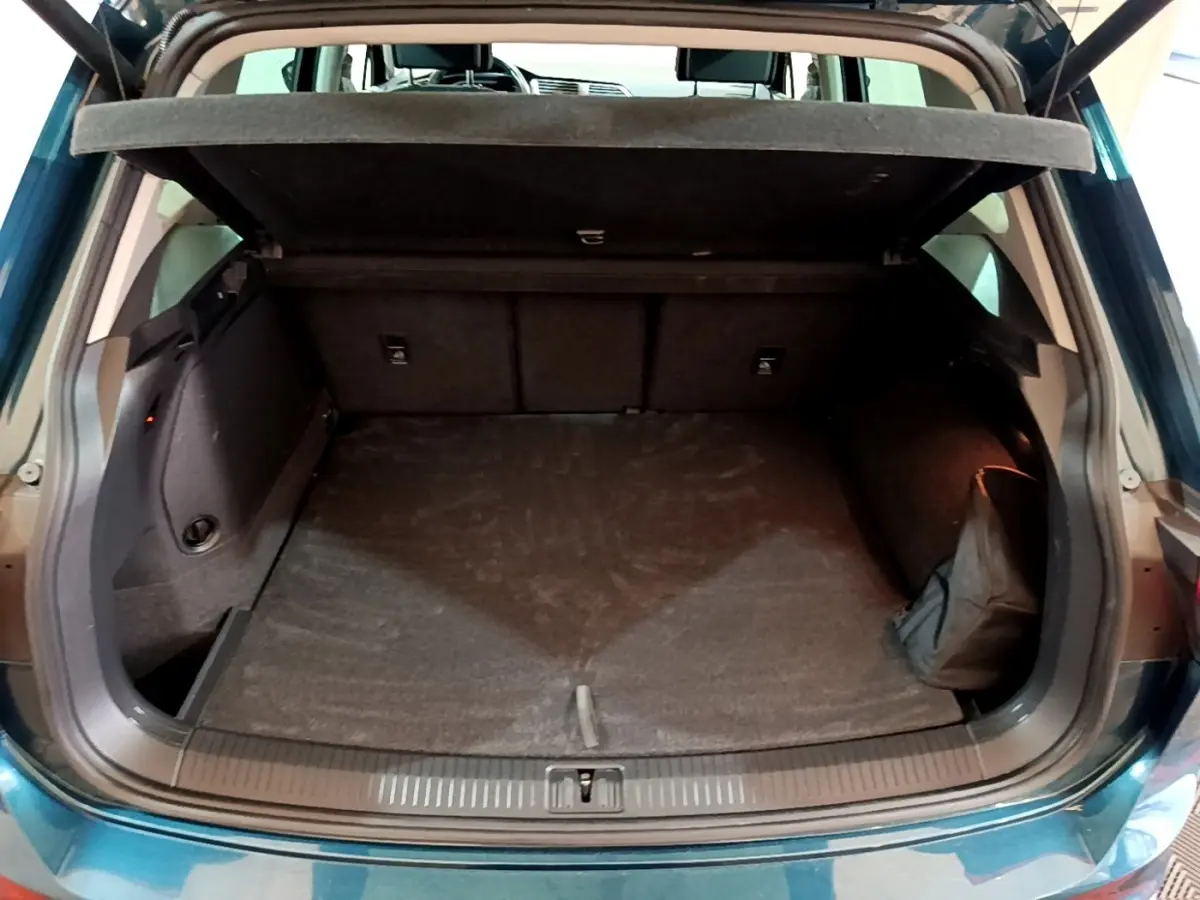 Coffre ouvert vu de l'arrière d'un Volkswagen Tiguan bleu, montrant un espace de rangement vide et la tablette cache-bagages.
