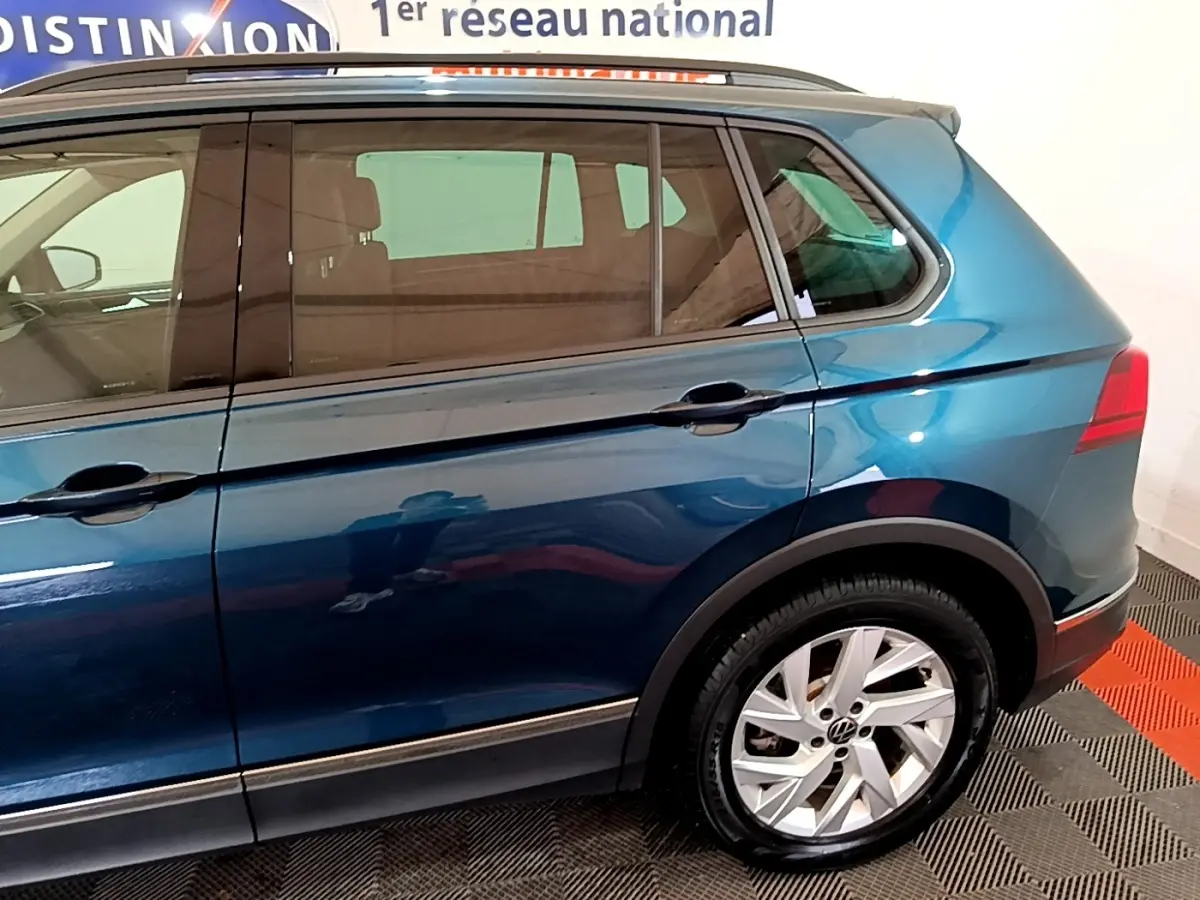 Vue latérale côté droit du Volkswagen Tiguan bleu hybride rechargeable, mettant en valeur la roue arrière et les vitres teintées.