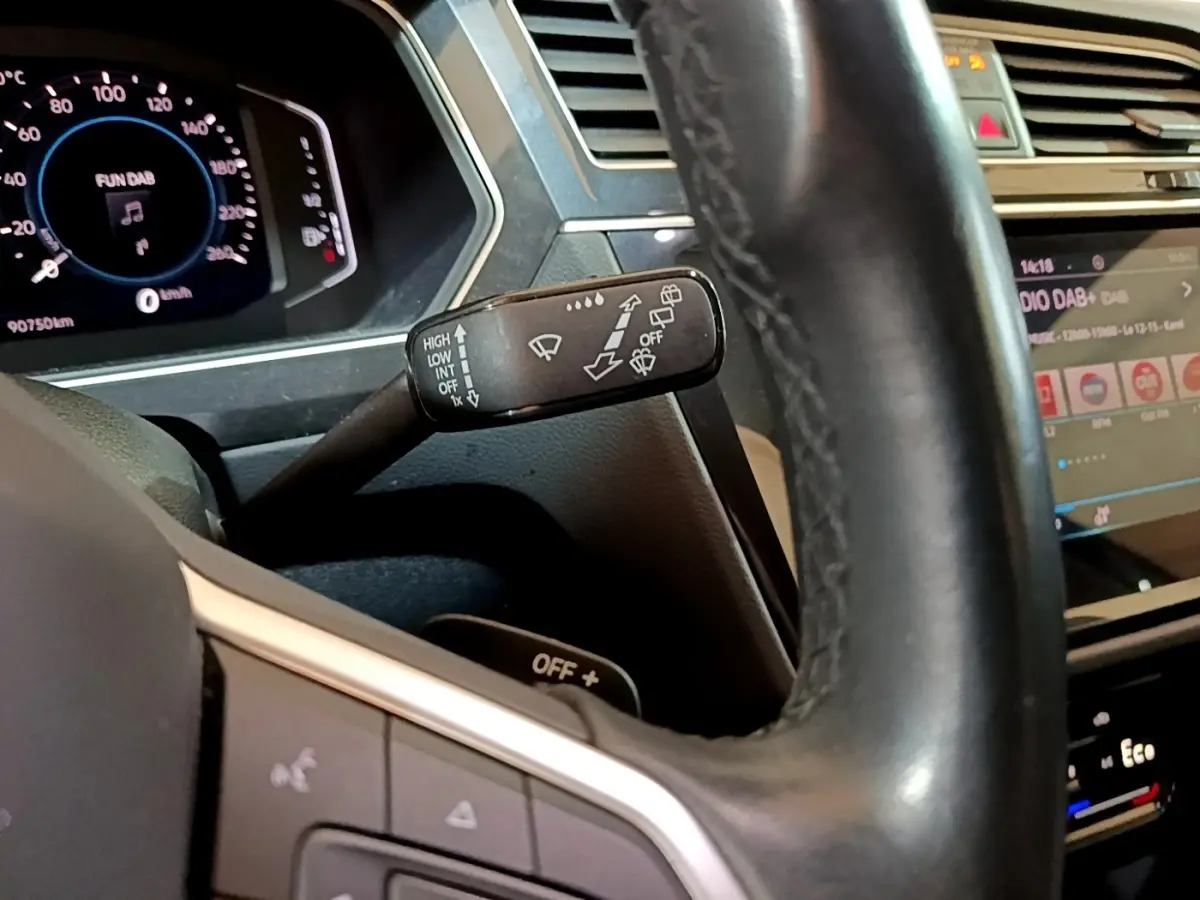 Gros plan sur le volant cuir noir et le commodo d’essuie-glace du Volkswagen Tiguan 1.4 eHybrid bleu, tableau de bord digital visible.