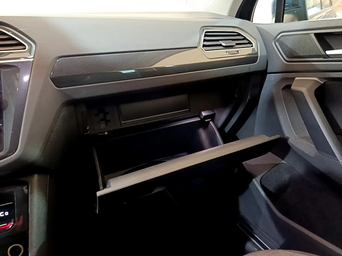 Vue intérieure côté passager du Volkswagen Tiguan bleu 2021, boîte à gants ouverte et tableau de bord noir.