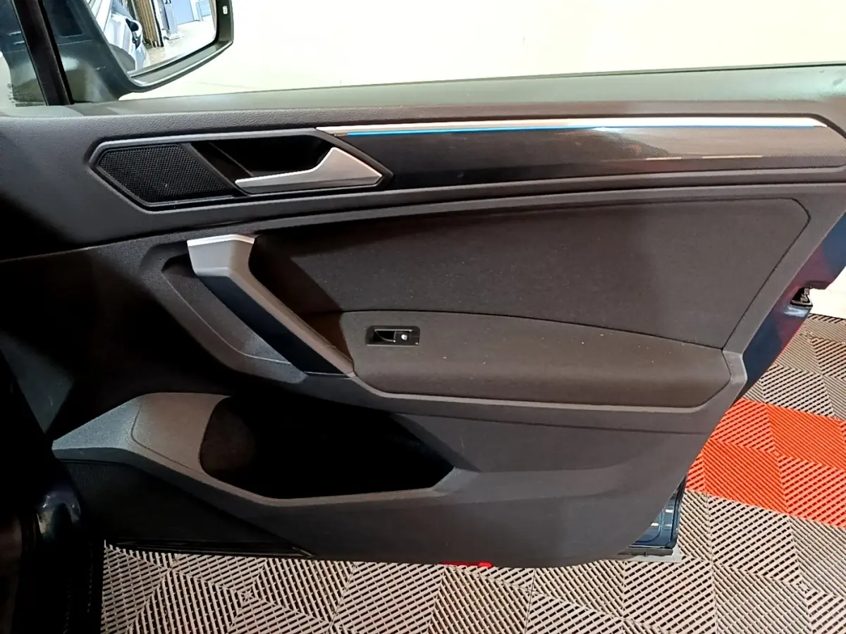 Vue intérieure côté gauche de la porte avant d’un Volkswagen Tiguan bleu, avec éclairage d’ambiance bleu fin.