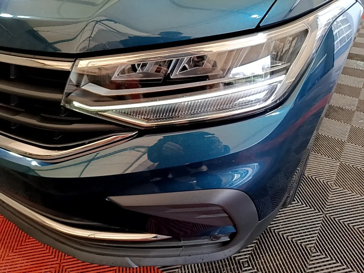 Gros plan sur le phare avant droit bleu métallisé du Volkswagen Tiguan 1.4 eHybrid avec calandre chromée.