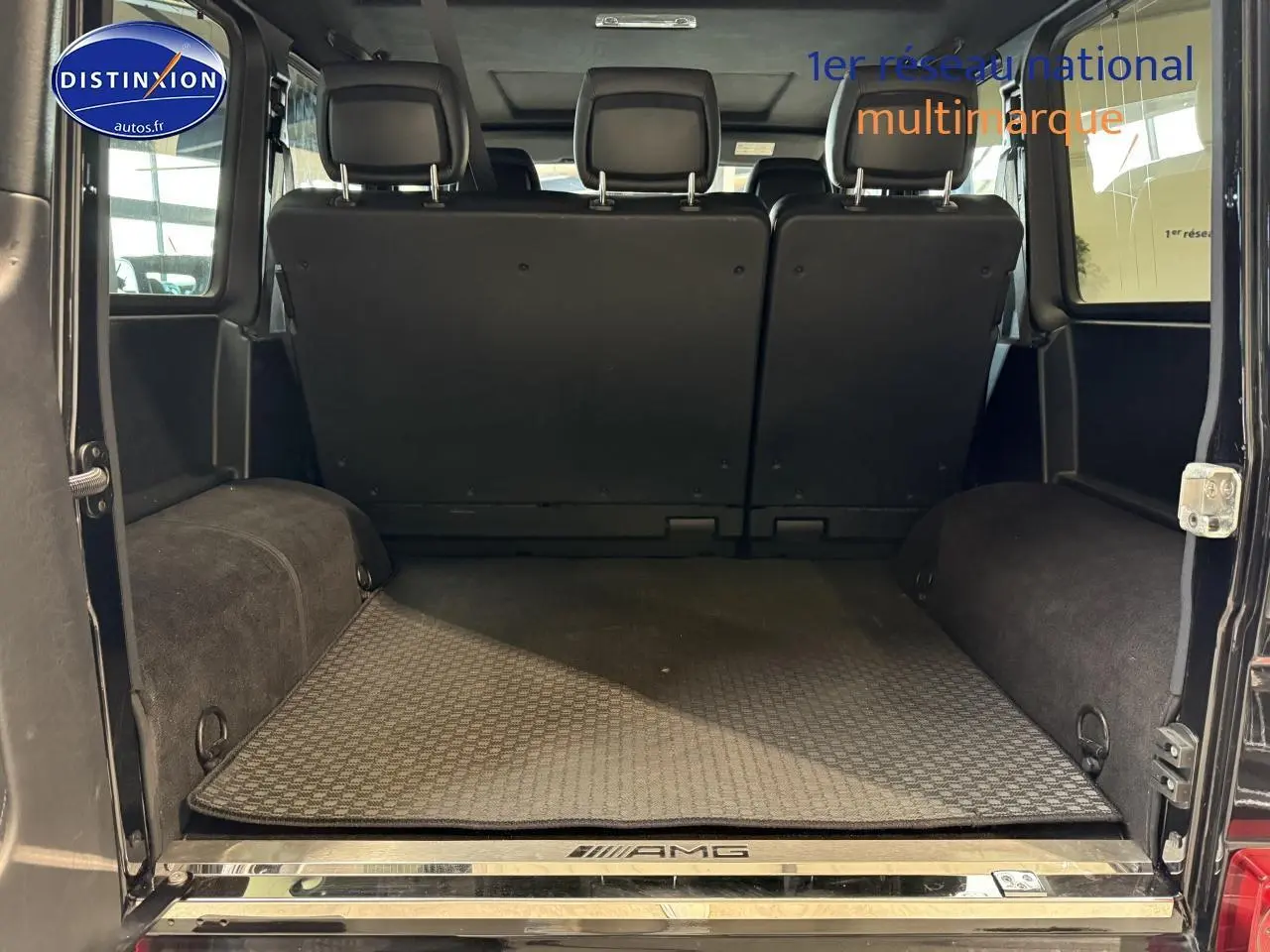 Coffre ouvert vu de l'arrière d'un Mercedes Classe G 5.5 63 AMG noir avec tapis AMG et banquette arrière relevée.