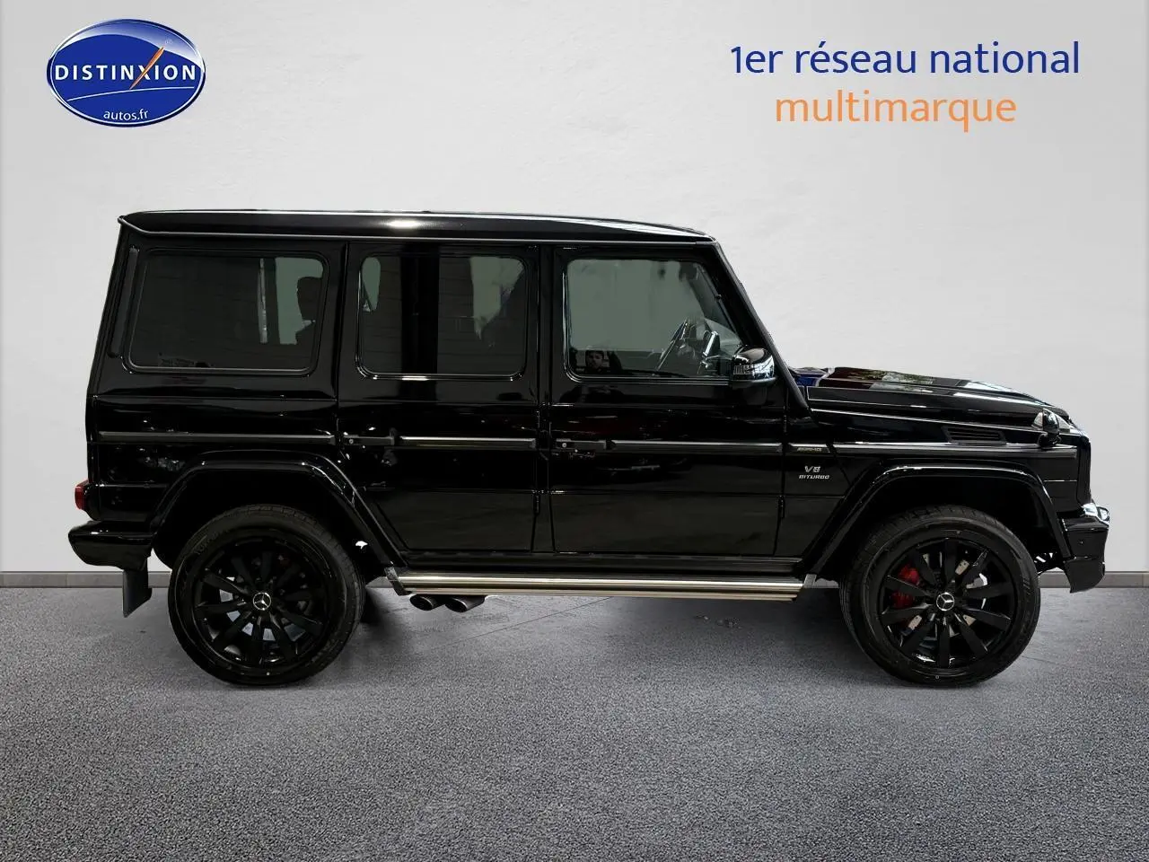 Profil côté gauche d'un Mercedes Classe G 5.5 63 AMG noir avec jantes noires et sorties d'échappement latérales chromées.