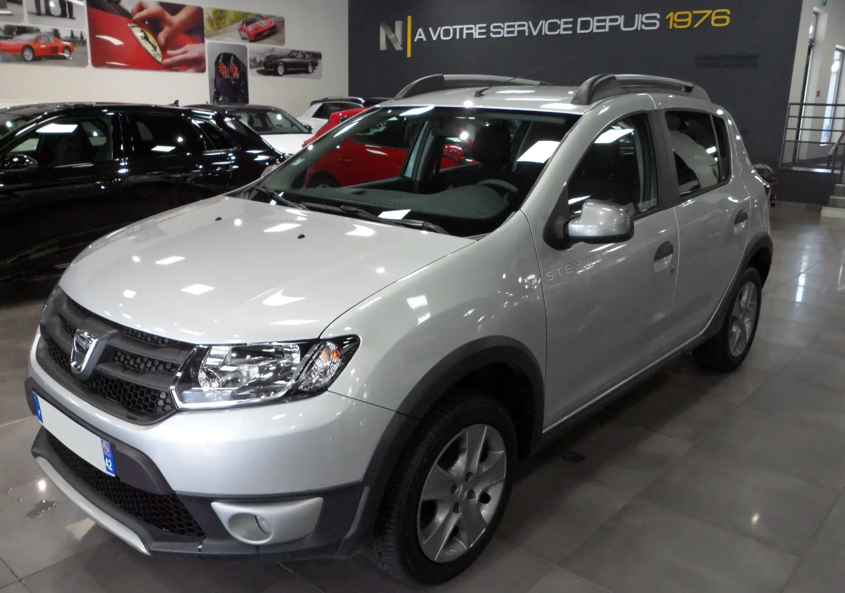 Dacia Sandero Stepway gris platine vue 3/4 avant droit en intérieur avec barres de toit et jantes alliage.