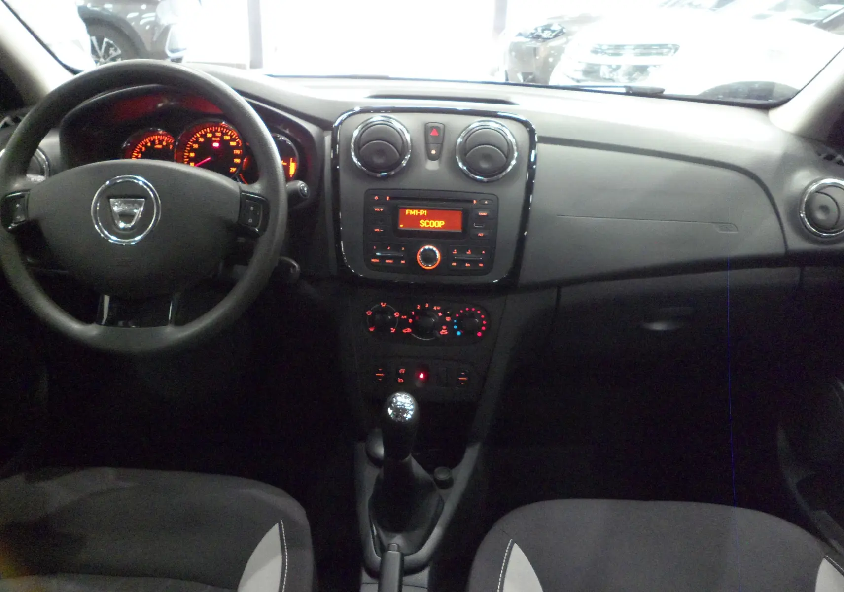 Vue intérieure frontale du tableau de bord et volant d'une Dacia Sandero Stepway 2016 avec commandes manuelles et affichage radio orange.