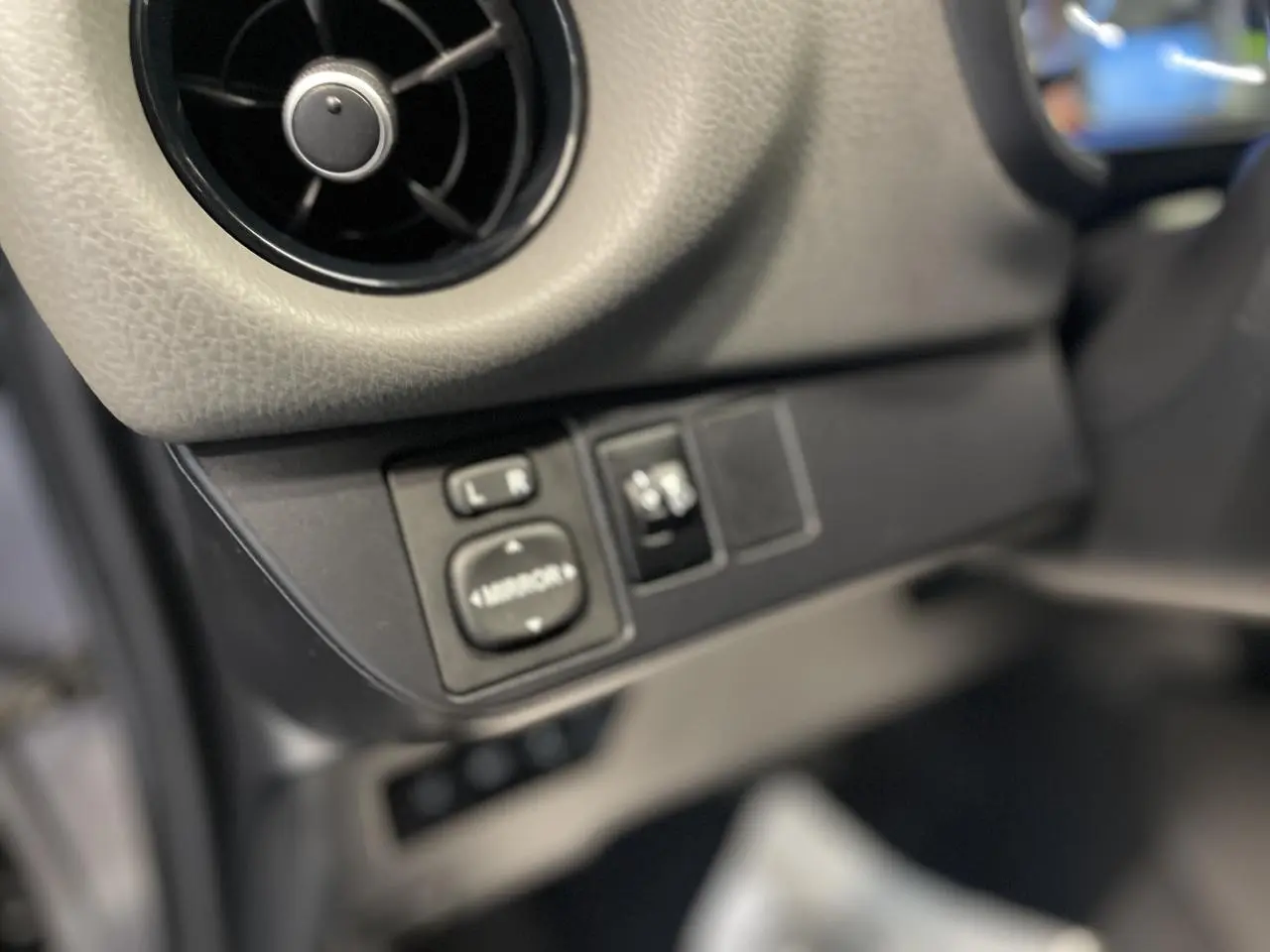 Détail du tableau de bord côté gauche avec commandes de réglage des rétroviseurs dans une Toyota Yaris hybride gris foncé.