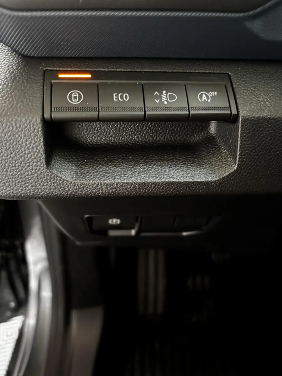 Gros plan sur les boutons de contrôle du tableau de bord du Dacia Bigster gris foncé, avec témoin orange allumé.