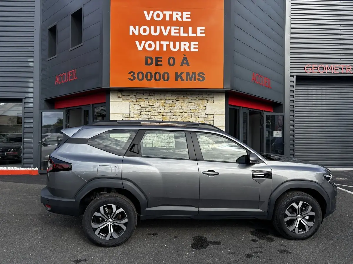 Profil droit du Dacia Bigster gris foncé 2025 avec jantes alliage et barres de toit noires visibles.
