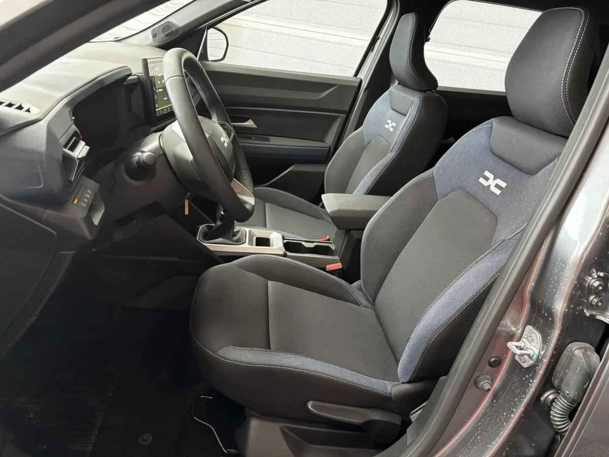 Intérieur avant droit du Dacia Bigster gris foncé, sièges tissu bi-ton avec logo DC et volant multifonctions.