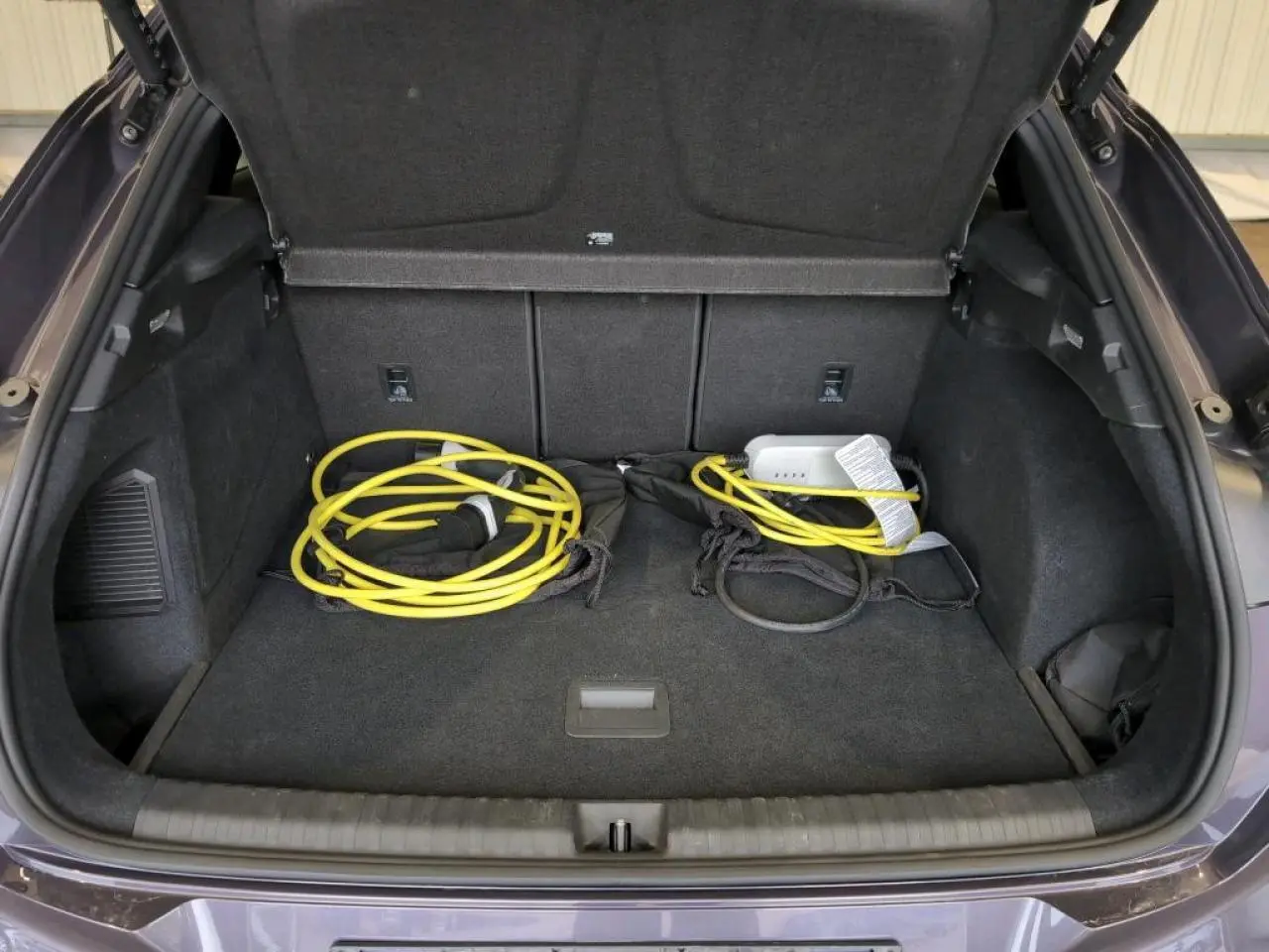 Coffre ouvert du CUPRA TERRAMAR 2024 Dark Void avec câble de recharge jaune visible sur la moquette noire.