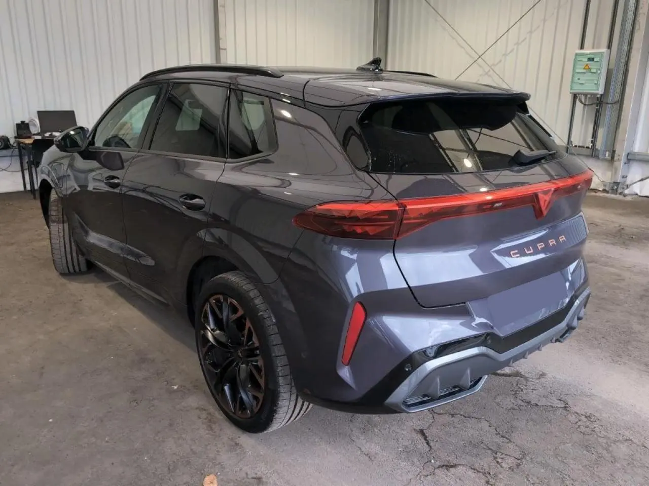 Vue 3/4 arrière droite du CUPRA TERRAMAR 2024 Dark Void avec jantes cuivrées et hayon électrique en intérieur d'atelier.
