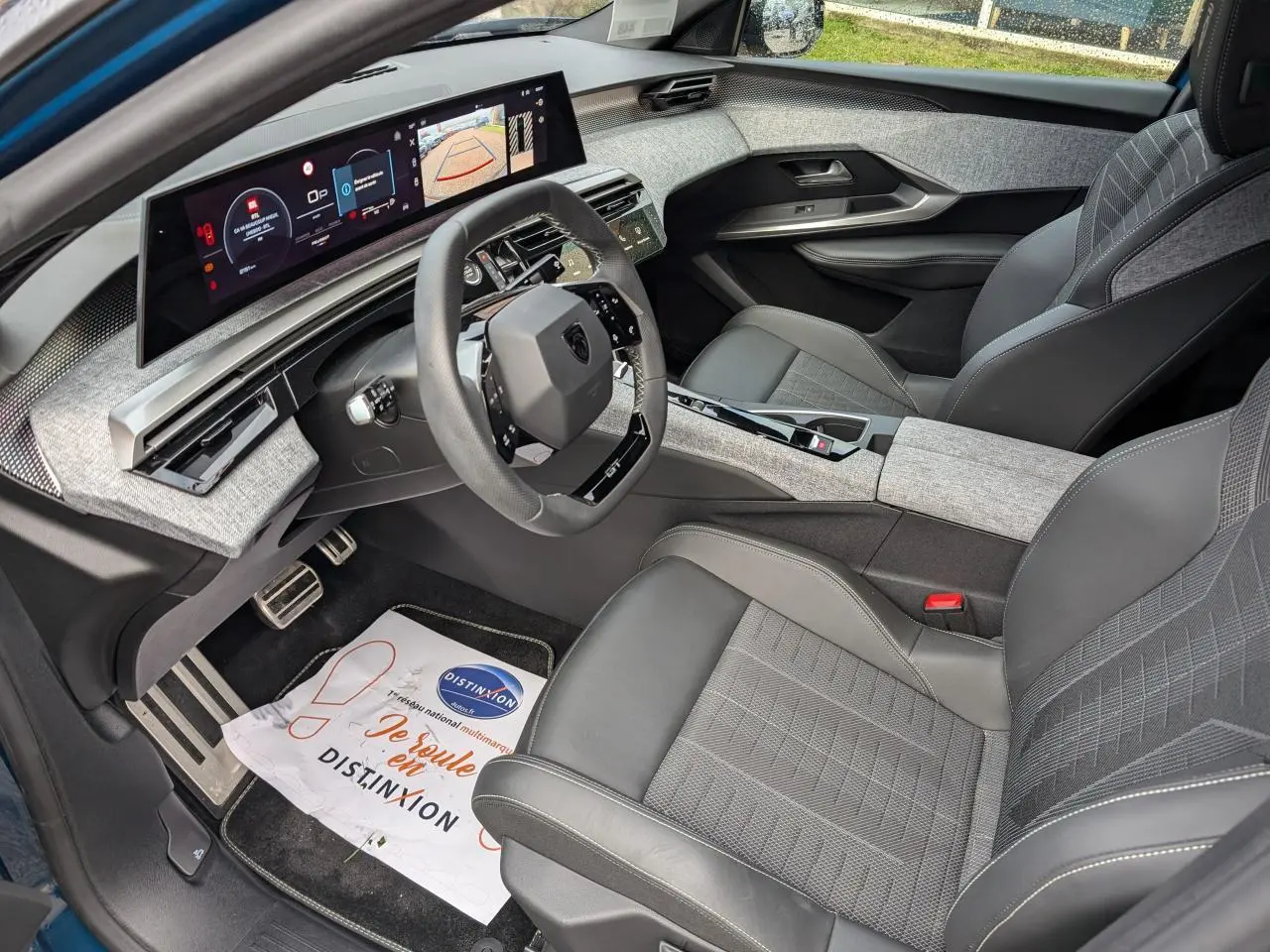 Vue intérieure côté conducteur du Peugeot 3008 Hybrid 2025 avec sellerie tissu gris et tableau de bord numérique panoramique.