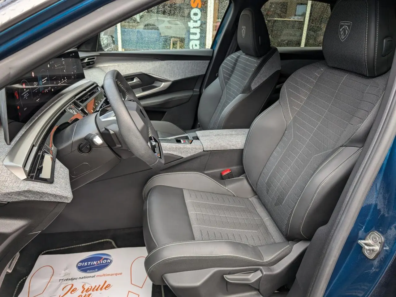 Vue intérieure côté conducteur du Peugeot 3008 Hybrid 2025 bleu métallisé, avec sièges tissu et cuir gris et tableau de bord numérique.