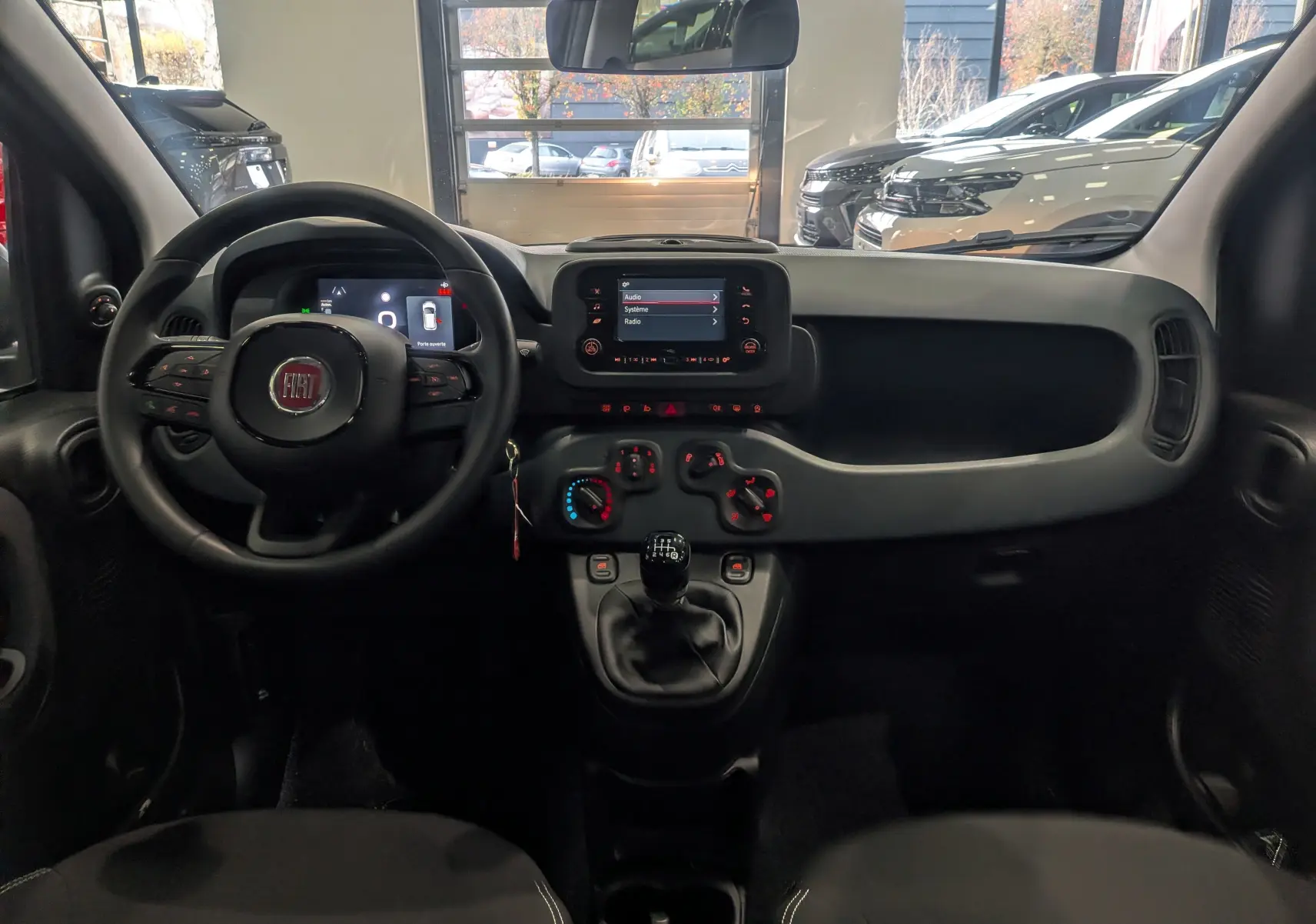 Vue intérieure frontale du tableau de bord noir de la Fiat Panda 1.0 Hybrid 2025 avec écran tactile et levier de vitesse manuel.