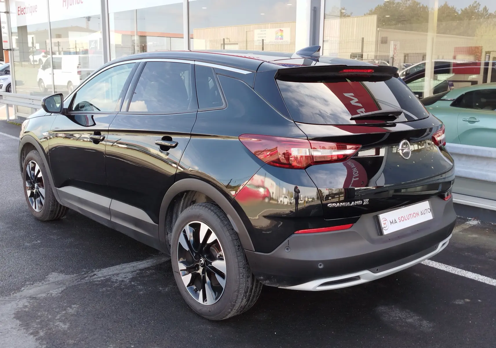 Vue 3/4 arrière droite d’un Opel Grandland X noir diamant avec jantes bi-ton et vitres teintées, stationné devant un showroom.