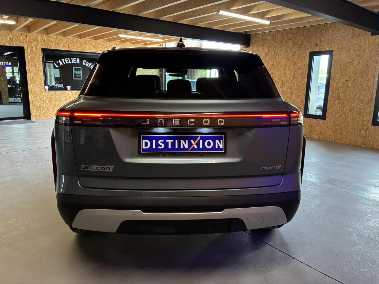 Vue arrière du SUV JAECOO J7 gris olive avec bandeau lumineux rouge et logo lumineux dans un garage.