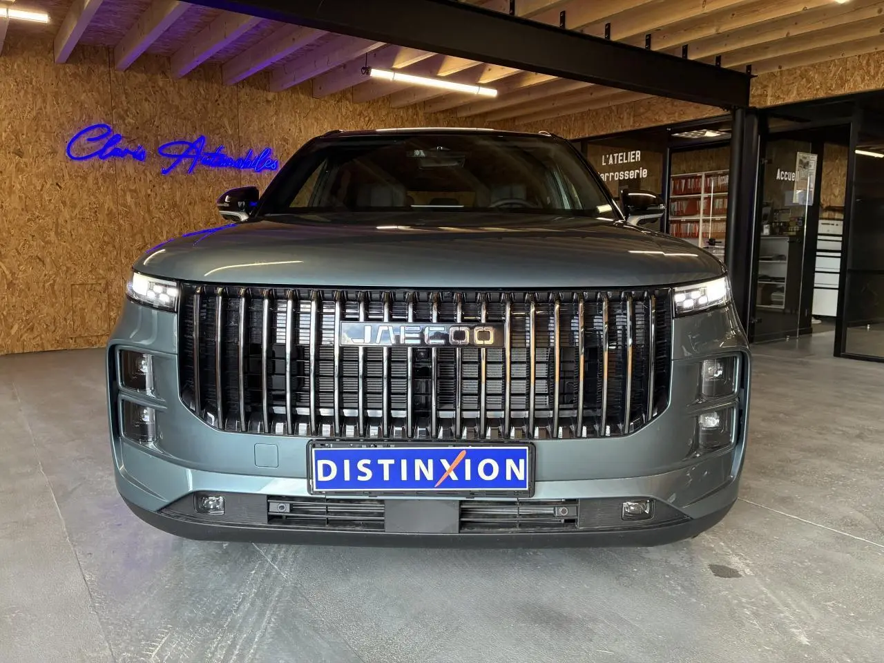 Vue frontale du SUV JAECOO J7 gris olive avec calandre verticale noire et toit noir dans un showroom.