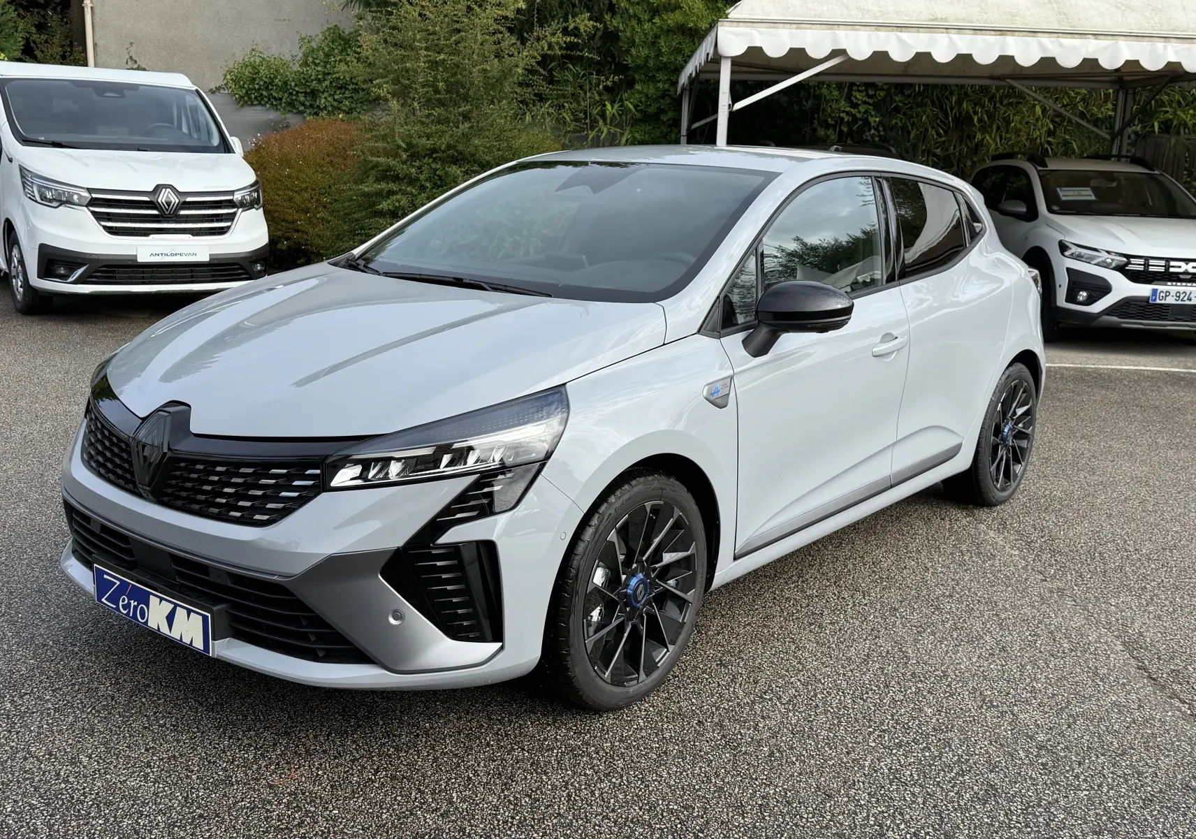 Renault Clio V 1.6 E-TECH gris Rafale vue 3/4 avant droit avec jantes noires et détails Alpine sur parking.