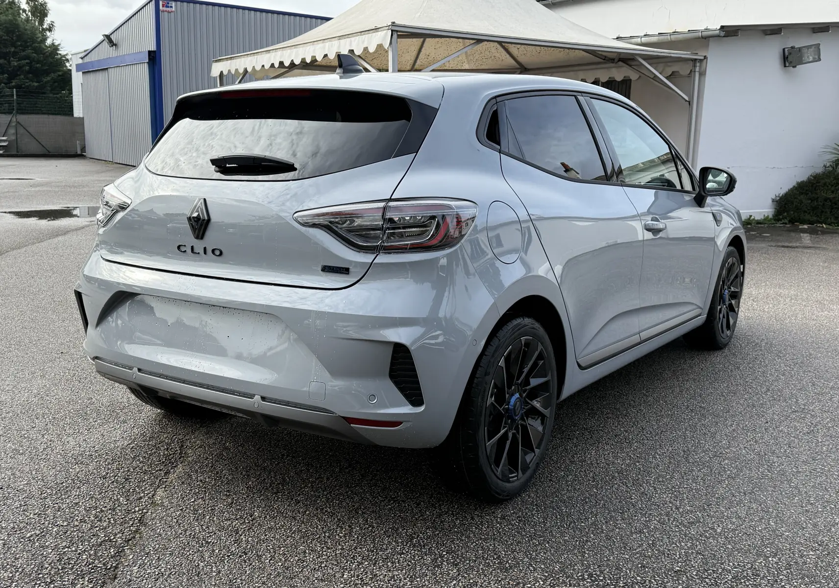 Renault Clio V gris Rafale vue 3/4 arrière droit, avec jantes noires et vitres teintées sur parking extérieur.