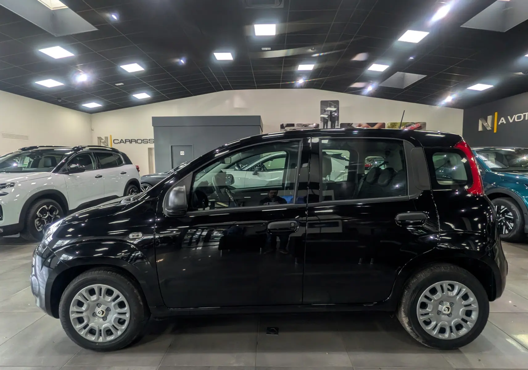 Vue de profil côté gauche d'une FIAT Panda 1.0 70 CH Hybrid City noire, en intérieur showroom avec jantes argentées.