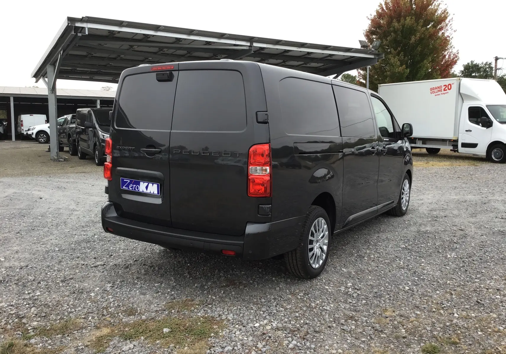 Vue 3/4 arrière droite d’un Peugeot Expert cabine approfondie gris titane avec vitres arrière opaques sur un parking.