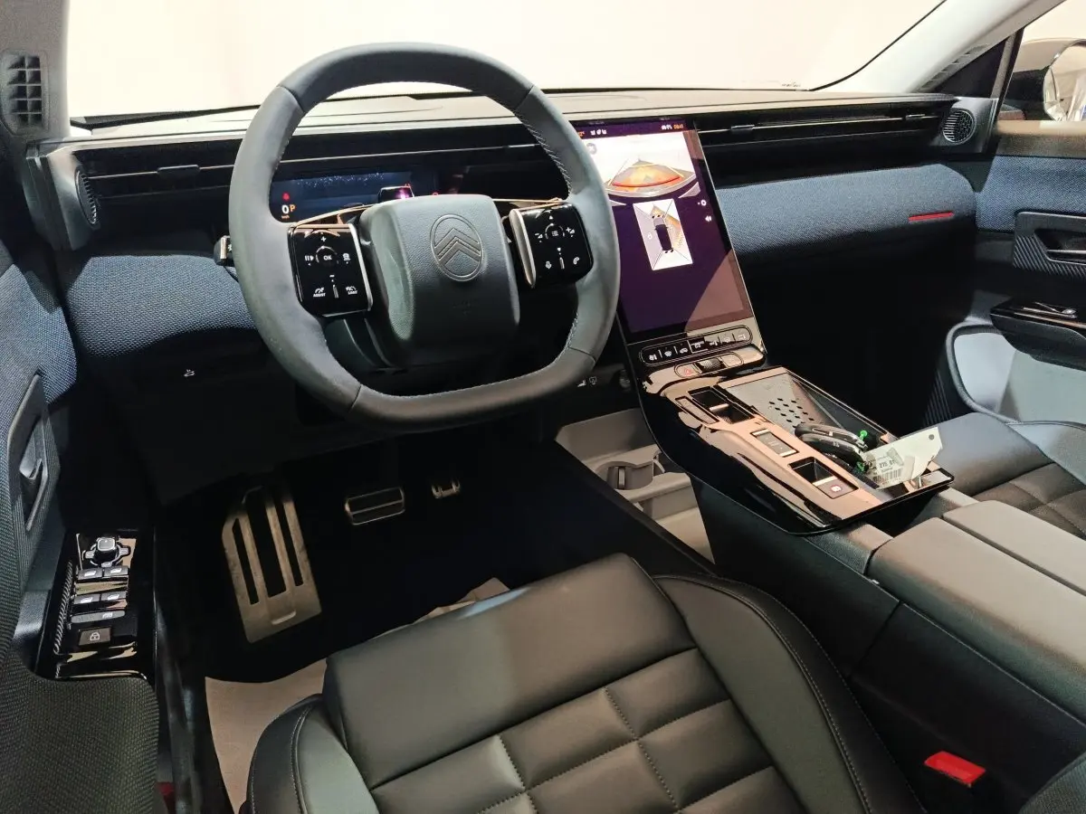 Intérieur avant du Citroën C5 Hybride 2026, vue conducteur, volant cuir et grand écran tactile vertical noir.