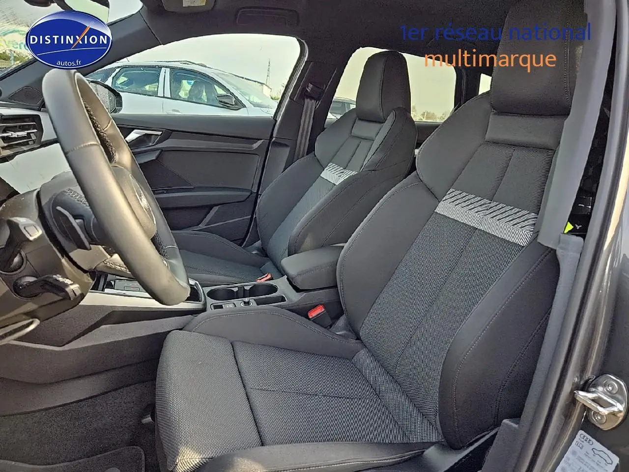 Intérieur avant de l'Audi A3 Sportback 2024 avec sièges sport gris et volant cuir multifonction visible côté conducteur.