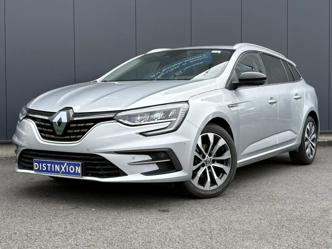 Renault Mégane Break gris clair en 3/4 avant droit, avec jantes alliage et calandre noire distinctive.