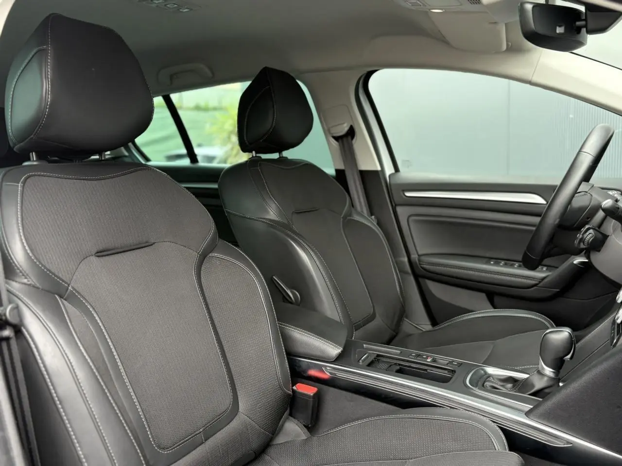 Vue intérieure du côté conducteur et passager avant de la Renault Mégane Break 2024 avec sellerie mixte similicuir et tissu carbone.