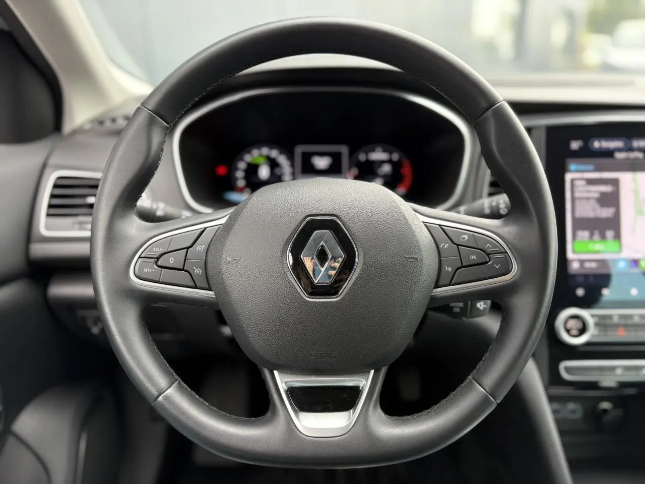 Volant en cuir noir de la Renault Mégane Break 2024 avec commandes intégrées et écran tactile GPS visible en arrière-plan.