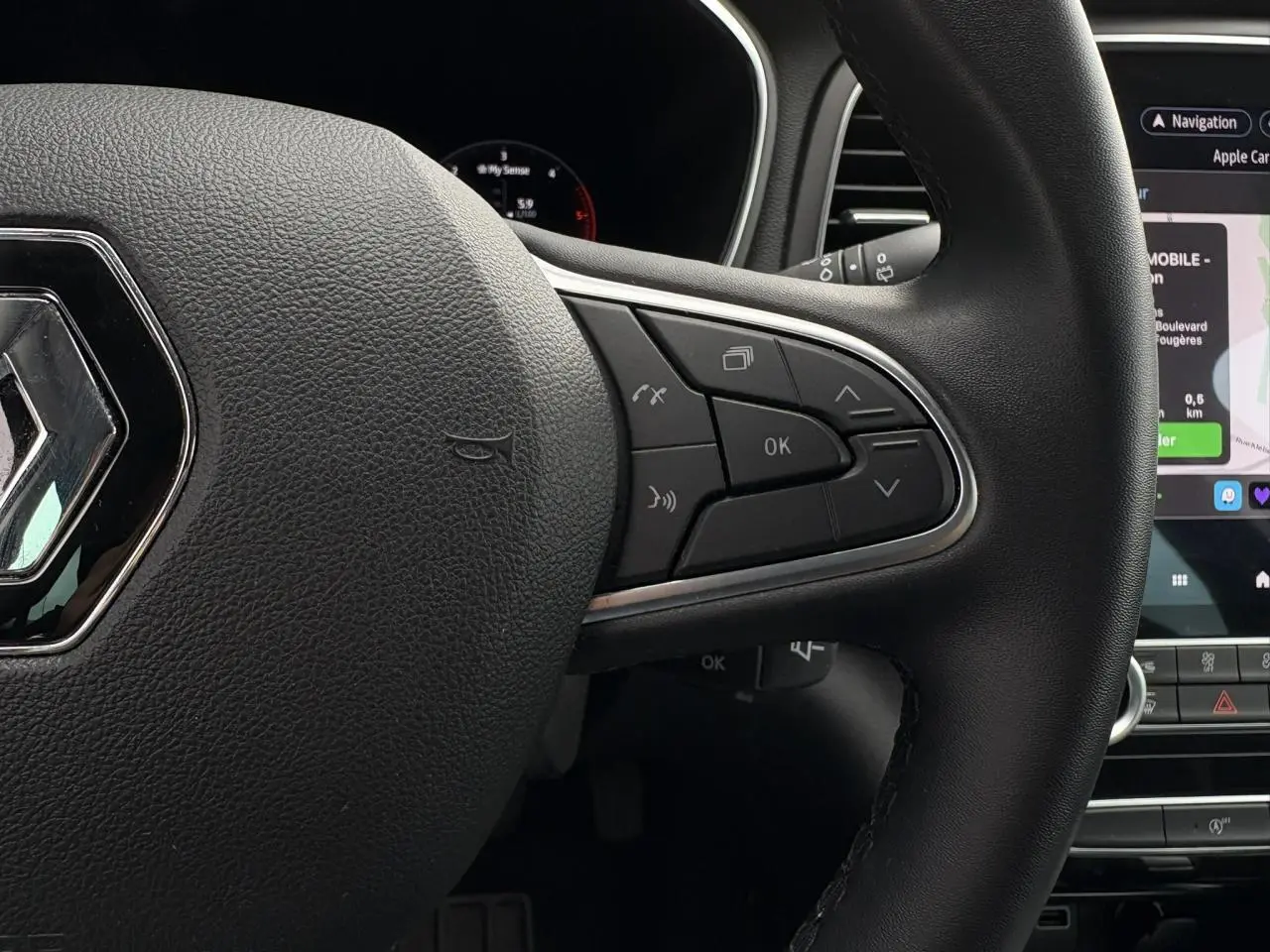 Gros plan sur le volant noir de la Renault Mégane Break 2024 avec commandes intégrées et écran tactile GPS visible.