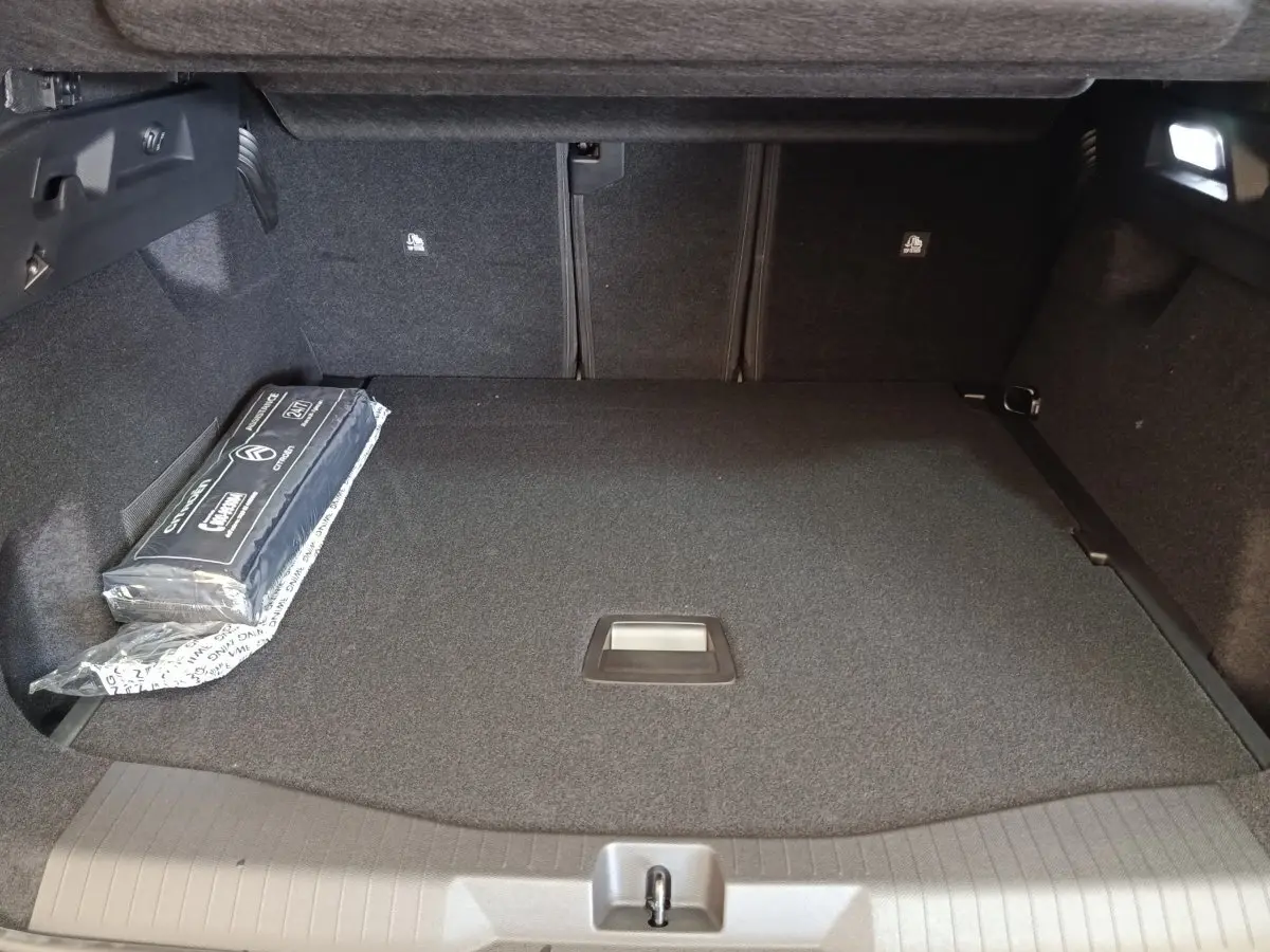 Vue intérieure du coffre spacieux et propre du Citroën C5 Hybride 2026, avec tapis gris et kit de sécurité sur le côté.