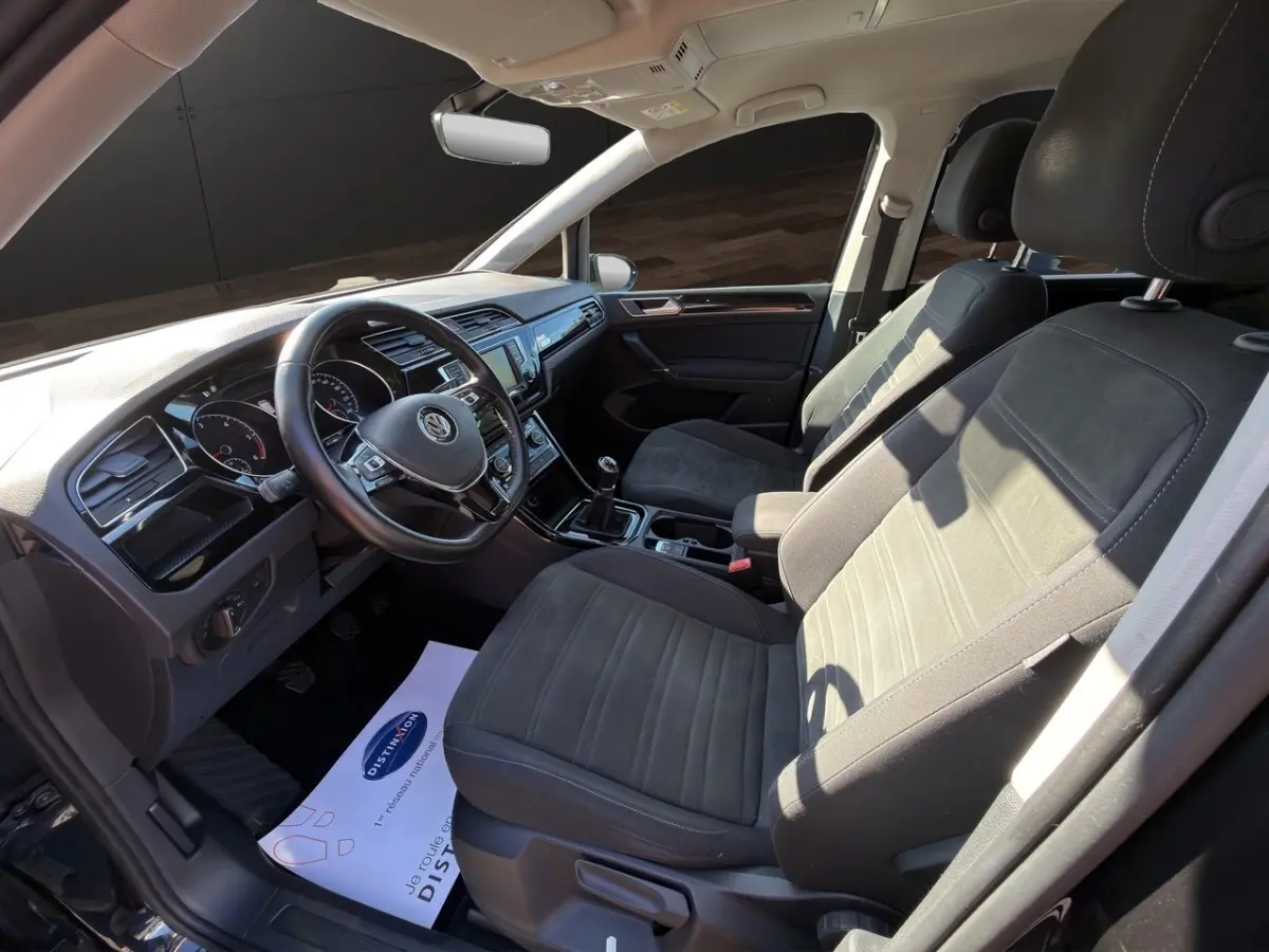 Vue intérieure côté conducteur du Volkswagen Touran 1.6 TDI noir, volant cuir alu multifonctions et boîte manuelle visible.