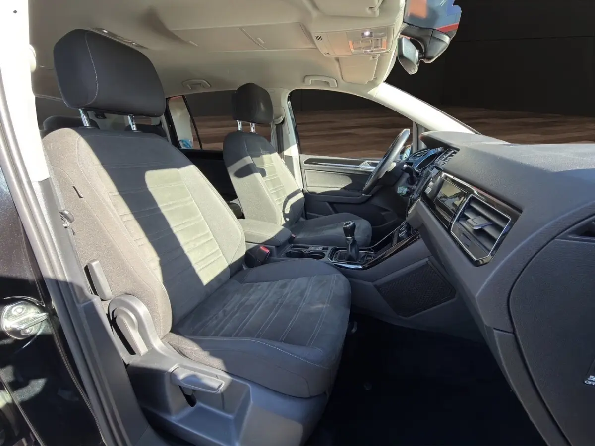Intérieur avant du Volkswagen Touran noir 2016, sièges tissu gris, volant multifonctions et boîte manuelle visible.