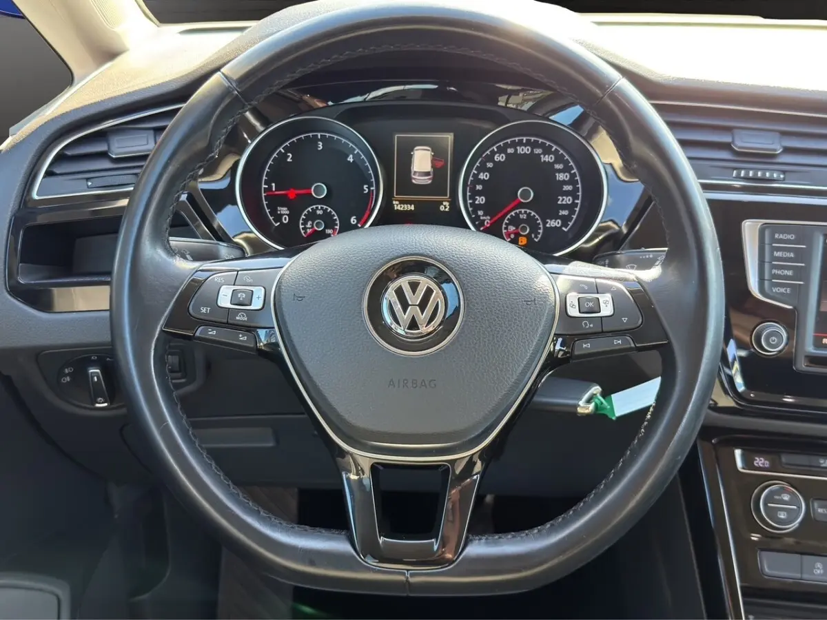 Vue intérieure centrée sur le volant cuir et alu noir du Volkswagen Touran 2016 avec tableau de bord et commandes visibles.