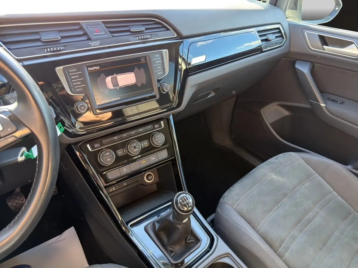 Intérieur avant droit du Volkswagen Touran noir 2016, avec tableau de bord, écran tactile et levier de vitesse manuel visible.
