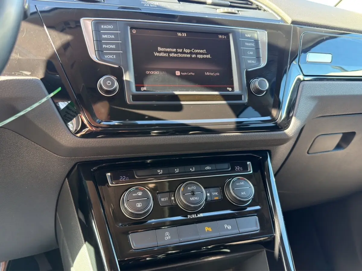 Tableau de bord noir du Volkswagen Touran 2016 avec écran tactile central et commandes climatisation en gros plan.